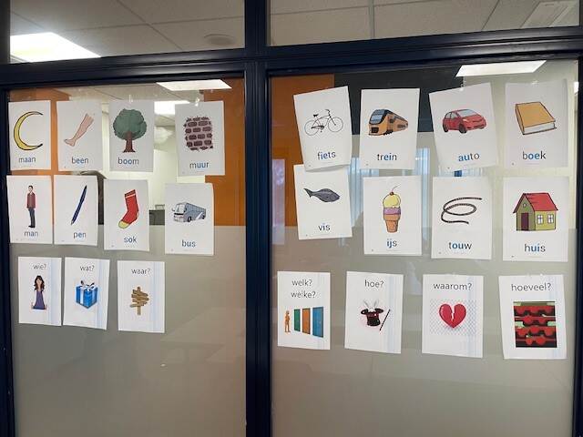 Afbeelding van een glazen wand met daarop plaatjes en het woord dat het plaatje omschrijft, als hulp bij het leren van nieuwe woorden.